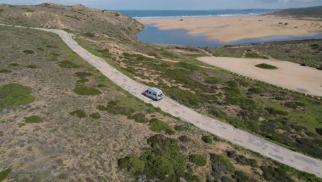 Aerial-View-Of-Van-Driving-Along-Road-Towards-Campsite-Beside-Bordeira-Beach-In-Portugal