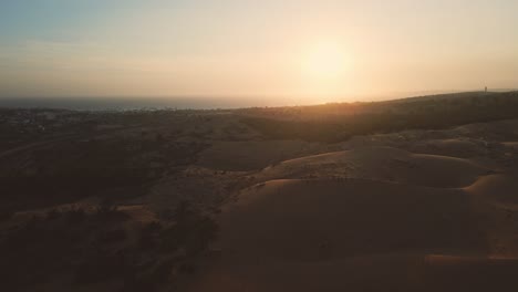 Scenic-aerial-pan-over-red-dunes-of-Mui-Ne-at-sunset,-tourists-exploring