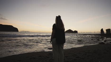 Woman-on-beach-looks-at-evening-horizon-by-rocky-Azores-coast,-pan