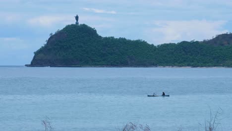 Lokaler-Timoresischer-Fischer-In-Einem-Traditionellen-Fischerkanuboot-Mit-Cristo-Rei-Statue-In-Der-Ferne-In-Der-Hauptstadt-Dili,-Timor-Leste,-Südostasien