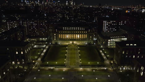 Vista-Aérea-Hacia-La-Biblioteca-Mayordomo-Iluminada-En-La-Universidad-De-Colombia-Con-El-Horizonte-De-Manhattan-En-El-Fondo