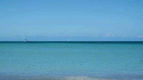 Ein-Segelkatamaran-überquert-Den-Horizont-über-Tropischem-Blauem-Und-Türkisfarbenem-Wasser-In-Der-Karibik