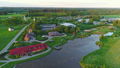 Small-town-in-rural-Latvia-with-a-park-and-reflective-lake,-lush-green,-aerial