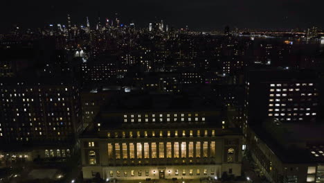 Flying-over-the-Butler-Library-towards-the-Manhattan-skyscrapers-,-night-in-NYC,-USA---Aerial-view