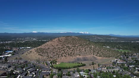 Drone-shot-of-Pilot-Butte-in-Bend,-Oregon-with-mountain-range-in-the-distance