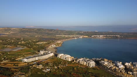 Drone-Volando-Hacia-La-Playa-De-Mellieha-Desde-Lejos-En-Una-Hermosa-Mañana-En-Malta