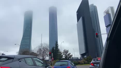 Cars-stopped-with-red-traffic-light-in-front-of-famous-four-towers-of-Madrid-covered-by-fog