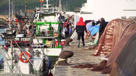 Slow-motion-shot-of-fisherman-walking-with-large-fishing-boats-docked-in-Puerto-Barbate