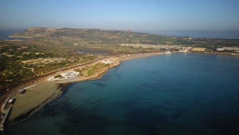 Drone-Orbita-Alrededor-De-La-Playa-De-Mellieha-Desde-Lejos-En-Una-Hermosa-Mañana-En-Malta