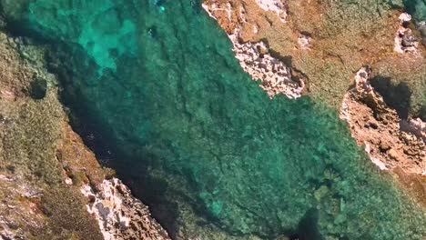 Drone-shot-rotating-downwards-towards-divers-in-crystal-clear-seas-in-Cirkewwa-Malta