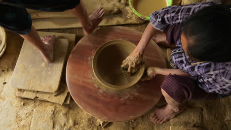 Top-down-footage-of-two-Asian-women-performing-traditional-pottery-on-a-foot-powered-turning-table,-capturing-the-beauty-and-cultural-significance-of-the-craft
