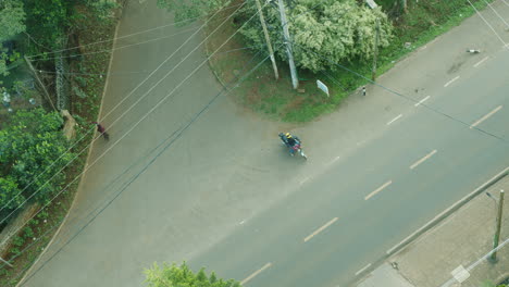 Aerial-view-from-above-of-a-motorcycle-entering-a-rural-road-in-Kenya,-Africa