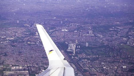 Aerial-flyover-the-city-of-Jakarta,-over-the-wing-of-an-airplane