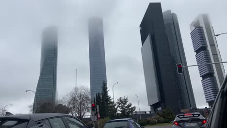 View-of-cars-stopped-at-a-traffic-light-with-a-view-of-the-4-towers-of-Madrid-covered-in-mist