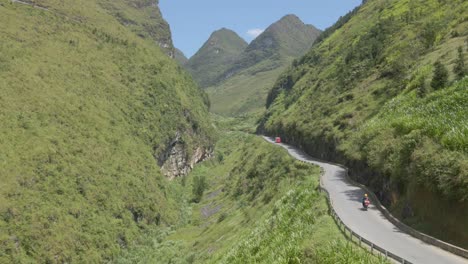 Drone-follow-up-a-motobike-on-mountain-path-toward-two-green-mountain-peaks-in-Ha-Giang-Viet-Nam