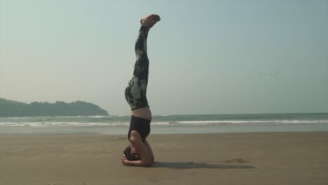 Mujer-Joven-En-Forma-Practicando-Un-Soporte-De-Cabeza-De-Yoga,-Salamba-Shirshasana,-En-Una-Cálida-Playa-Tropical