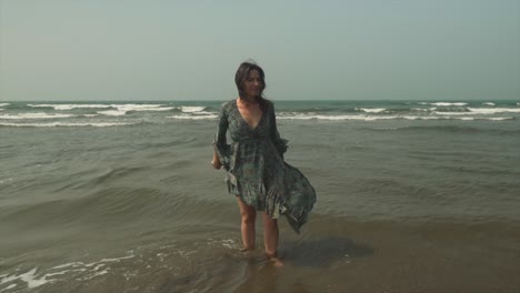 Woman-in-a-dress-looking-around-over-the-beach,-standing-in-the-sea