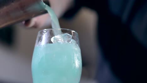 Bokeh-Aufnahme-Eines-Barkeepers,-Der-Einen-Leuchtend-Blauen-Cocktail-In-Ein-Glas-Gießt