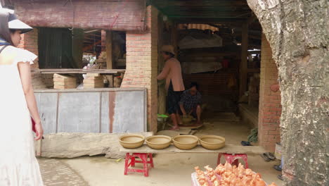 Tourists-visit-a-local-clay-shop-in-Thanh-Ha,-watching-craftswomen-making-bowls-while-clay-animals-figured-flutes-are-on-display,-capturing-the-essence-of-traditional-craftsmanship-and-local-culture