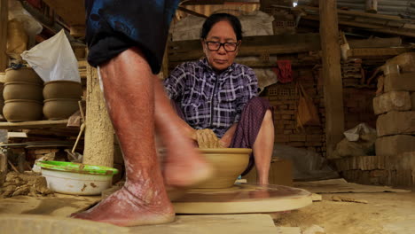 An-Asian-woman-finishes-a-big-bowl-on-a-foot-powered-turning-table,-showcasing-traditional-craftsmanship-and-artisanal-skills