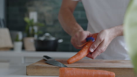 Mittlere-Aufnahme-Eines-Mannes,-Der-In-Einer-Modernen-Küche-Frische-Karotten-Mit-Einem-Messer-Schneidet