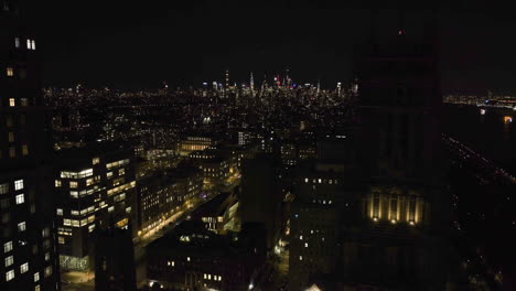 Aerial-view-flying-in-middle-of-the-Riverside-church-and-the-Claremont-hall,-towards-the-Manhattan-skyline,-night-in-NY,-USA