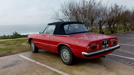 Lujoso-Coche-Rojo-Alfa-Romeo-Spider-Estacionado-En-Un-Parque-Con-El-Mar-Al-Fondo