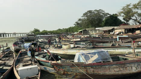 Im-Hafen-Von-Bandim-Vertäute-Hölzerne-Fischerboote,-Mit-Einigen-Fischern,-Im-Hintergrund-Sehr-Rudimentäre-Häuser-Mit-Zinkdächern