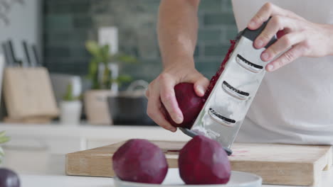 Medium-shot-of-a-man-grating-fresh-beetroot-with-a-grater-in-a-modern-kitchen