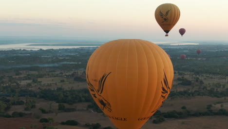 Reveal-of-group-of-Hot-Air-Ballons-behind-single-Yellow-Hot-Air-Balloon-,-Aerial-Sunrise-Shot,-Bagan,-Myanmar