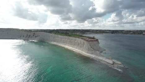 Rotating-Drone-Footage-Over-A-Limestone-Cliff-Side,-With-Tropical-Turquoise-Water,-Blue-Sky-And-Fluffy-White-Clouds,-Malta