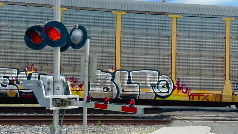 Railroad-crossing-arm-with-flashing-lights-with-Norfolk-Southern-train-on-tracks