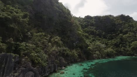 Fpv-drone-shot-of-cliff-jungle-by-turquoise-water-bay-in-Coron,-breathtaking-landscape