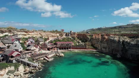 Luftaufnahme-über-Den-Themenpark-Popeye-Village-In-Malta-Mit-Felsiger-Küste-Und-Türkisfarbenem-Wasser