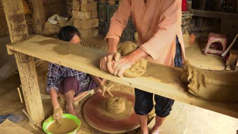 A-traditional-pottery-making-scene-in-Asia,-captured-in-a-downwards-pointed-footage-of-two-women-working-together-on-a-foot-powered-turning-table
