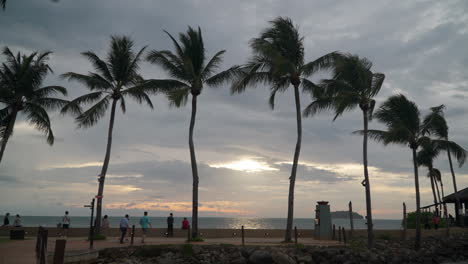 La-Gente-Disfruta-De-La-Majestuosa-Puesta-De-Sol-Sobre-El-Mar-En-El-Paseo-Marítimo-De-Tanjung-Aru---Cámara-Lenta,-Estableciendo-Una-Gran-Toma