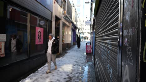 People-walking-down-snowy,-sunny-back-street-near-closed-shops
