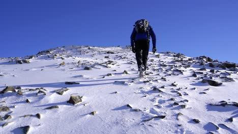 Male-hiker-walking-to-the-summit-of-the-Cuillin-Mountains-on-a-sunny-winter-day-in-Scotland
