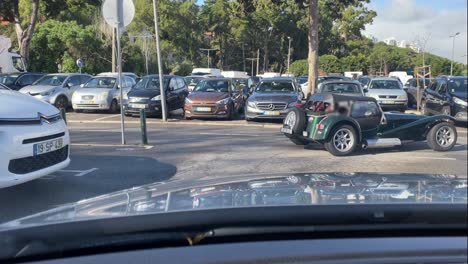 An-imposing-classic-American-car-exits-Cascais-market's-parking-lot-after-a-great-coffee,-its-vibrant-cherry-red-paint-shining-under-the-sun,-evoking-the-iconic-style-of-US-automotive-culture