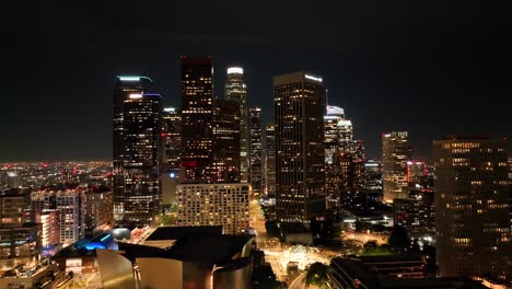 Aerial-view-approaching-illuminated-downtown-Los-Angeles-California-futuristic-city-skyline-at-night