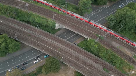 Birds-eye-view-of-a-railway-bridge-crossing-a-big-street-with-a-red-commuter-train-crossing-the-bridge-to-the-north