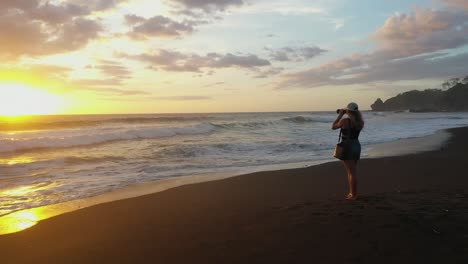 Woman-taking-photos-at-beach-during-sunset-in-tropics