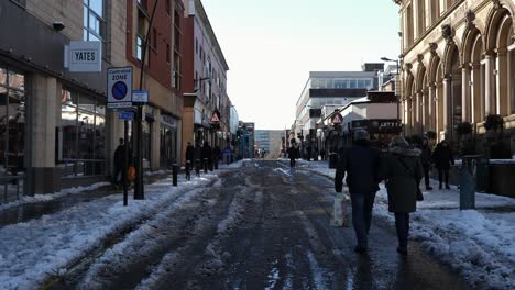 People-walking-on-snowy,-slushy-street-on-sunny-day,-Sheffield