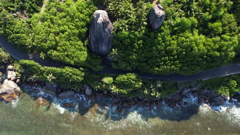 bird-eye-view-of-lush-vegetation,-huge-granite-rock-and-road-near-the-cliff-at-Anse-forbans-beach-Mahe-Seychelles