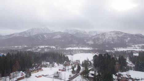 Backwards-drone-dolley-shot-of-snow-falling-in-Zakopane-with-the-high-winter-sport-mountains-in-the-background