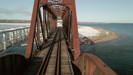 drone-flying-through-a-train-bridge-over-the-ocean-in-Chandler,-Québec,-Canada