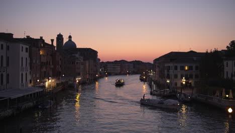 Wide-static-shot-of-boats-cruising-through-Canal-Grande-at-Twilight,-Venice,-Italy