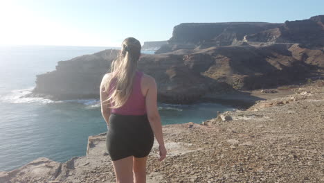 young-woman-walks-to-the-end-of-the-cliff-and-looks-at-the-beach-and-the-views