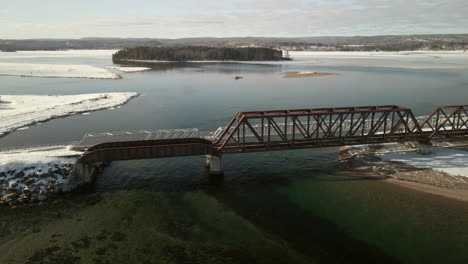 Drone-flying-over-a-train-bridge-going-over-the-ocean-in-Chandler,-Quebec,-Canada