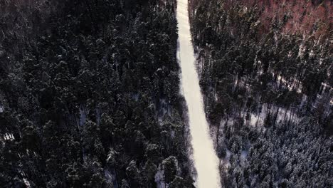 Aerial-view-of-a-drone-flying-over-a-forest-road-in-winter
